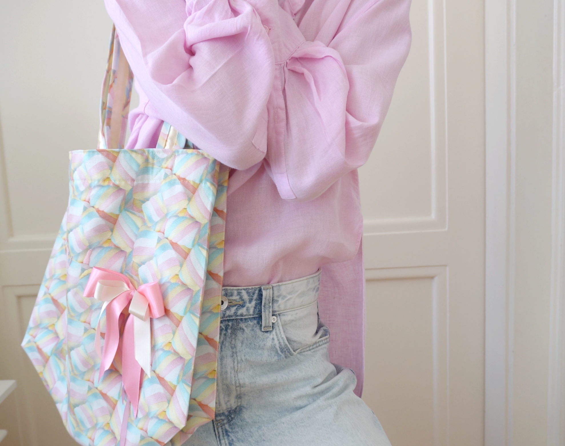 Person wearing a pink shirt with a colorful marshmallow tote bag over the shoulder against a neutral background