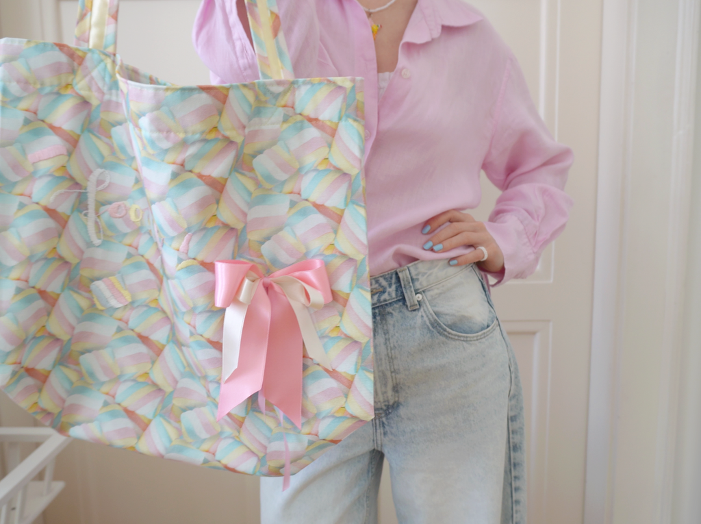 Person holding a colorful tote bag with a pink ribbon and marshmallow pattern