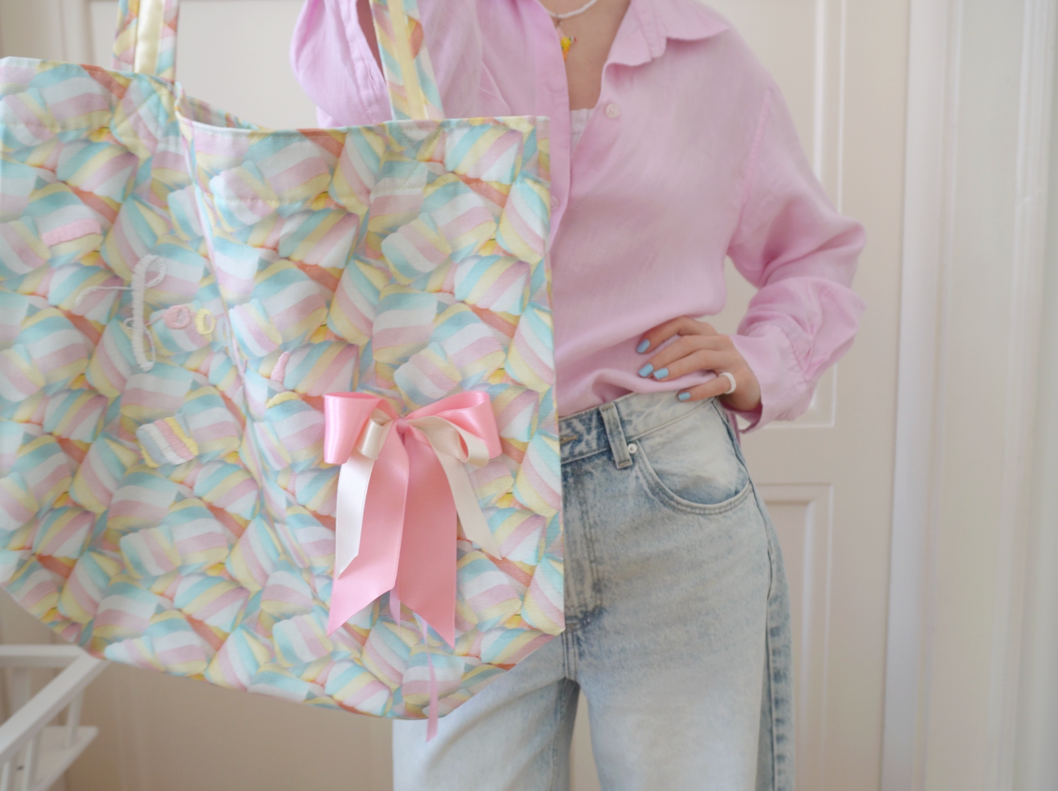 Person holding a colorful tote bag with a pink ribbon and marshmallow pattern