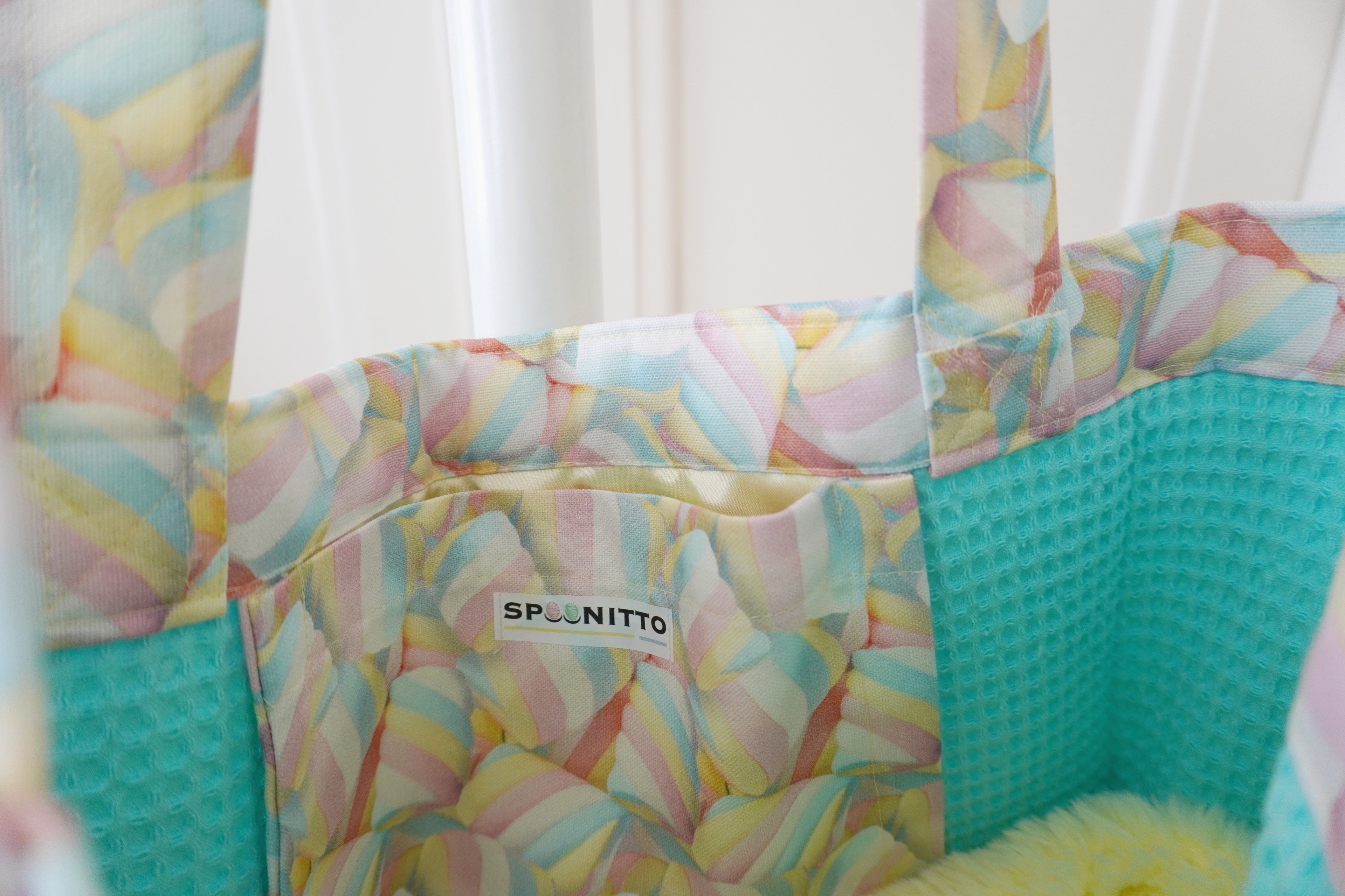Colorful tote bag pocket with 'SPOONITTO' branding against a white door background