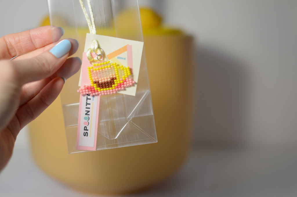 Handmade beaded ristretto coffee cup pendant in a clear bag with SPOONITTO branding.