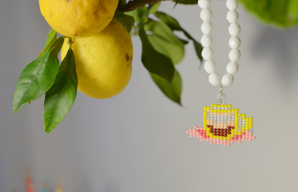 White beaded necklace with a ristretto coffee cup pendant next to lemons and leaves.