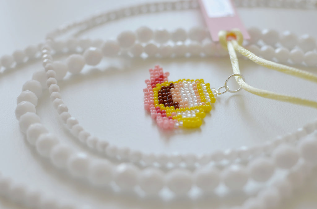 White beaded necklace with a small Italian coffee cup pendant on a white textured surface.