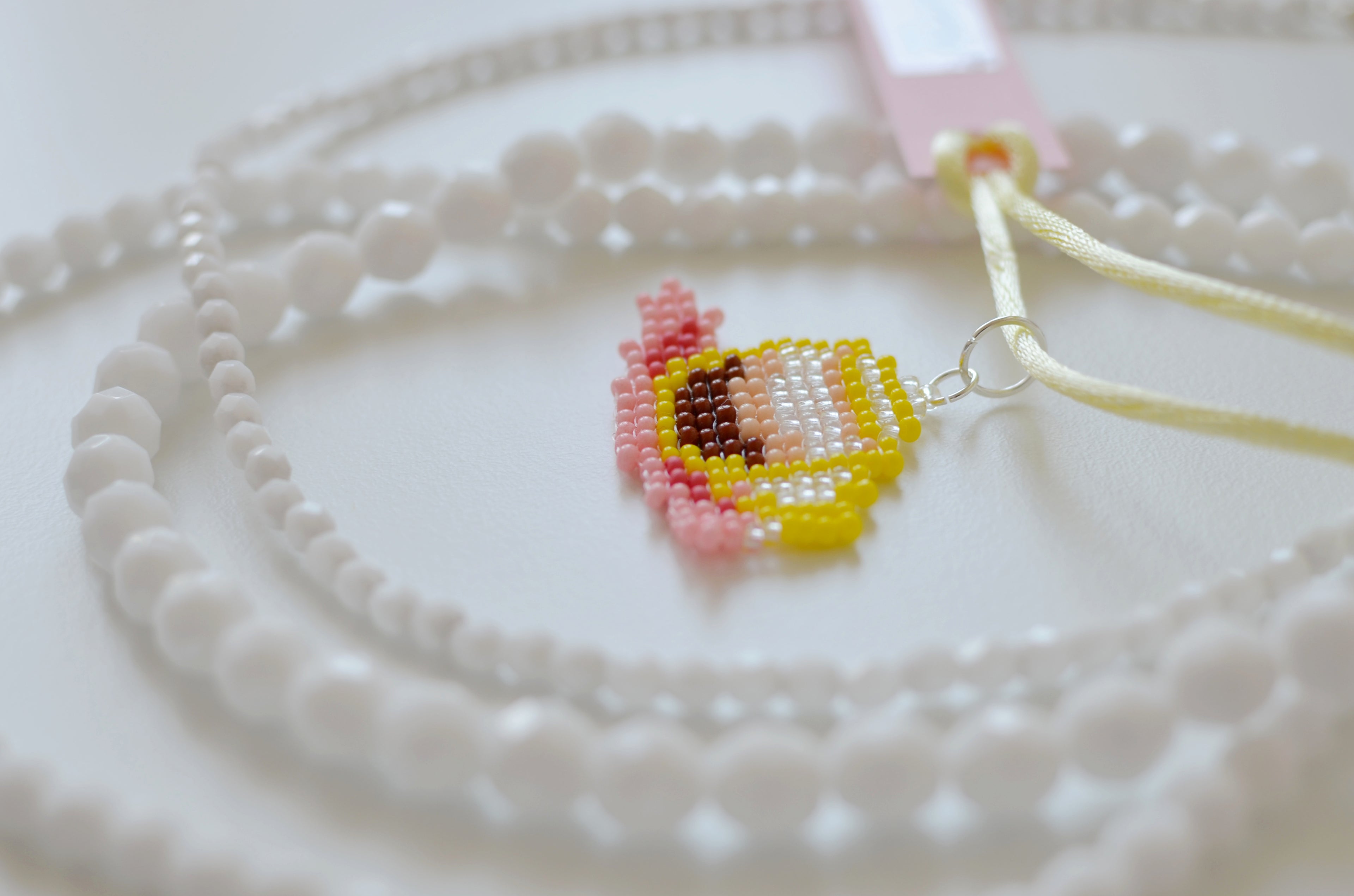 White beaded necklace with a small Italian coffee cup pendant on a white textured surface.