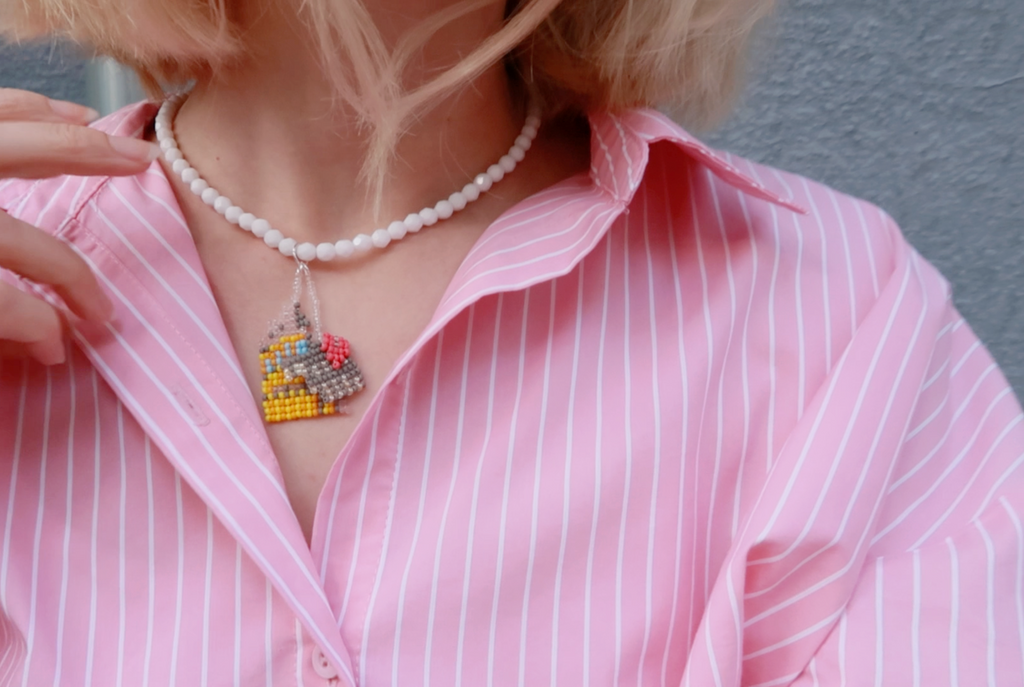 Person wearing a pink striped shirt with a white beaded necklace featuring a Colosseum pendant.