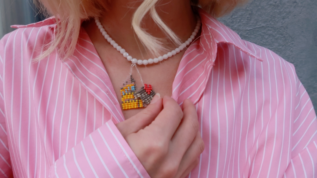 Person wearing a pink striped shirt with a romantic Rome-inspired Colosseum necklace.