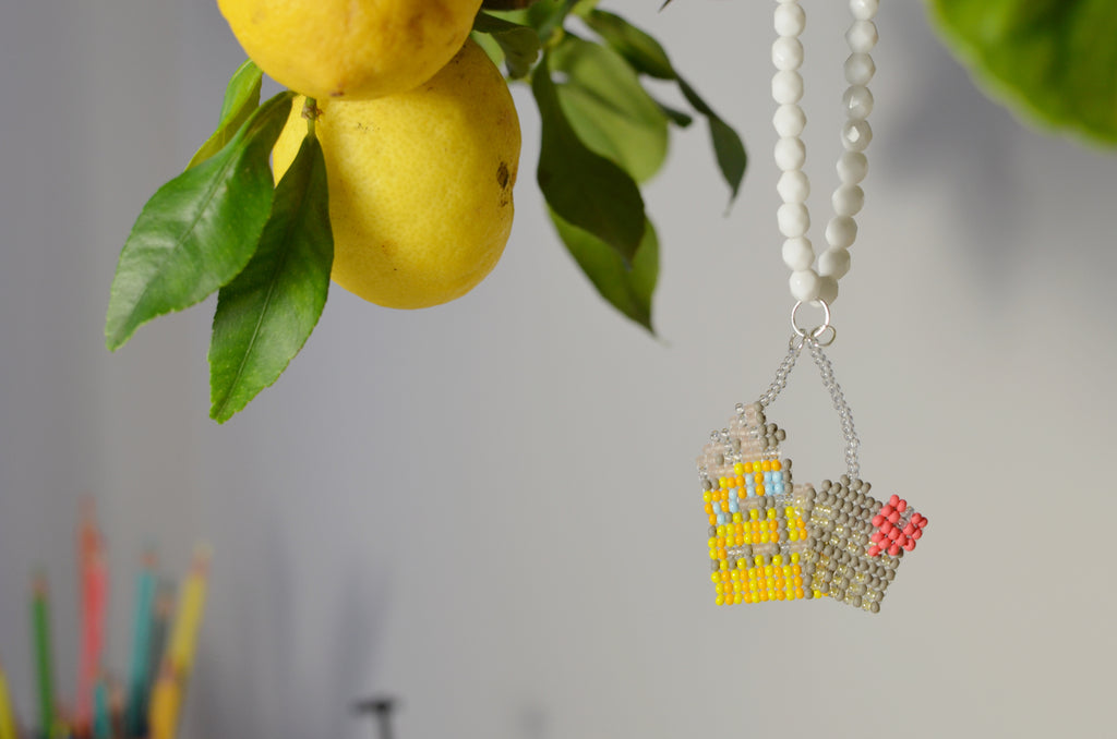 White beaded necklace with a Colosseum pendant next to lemons and leaves.