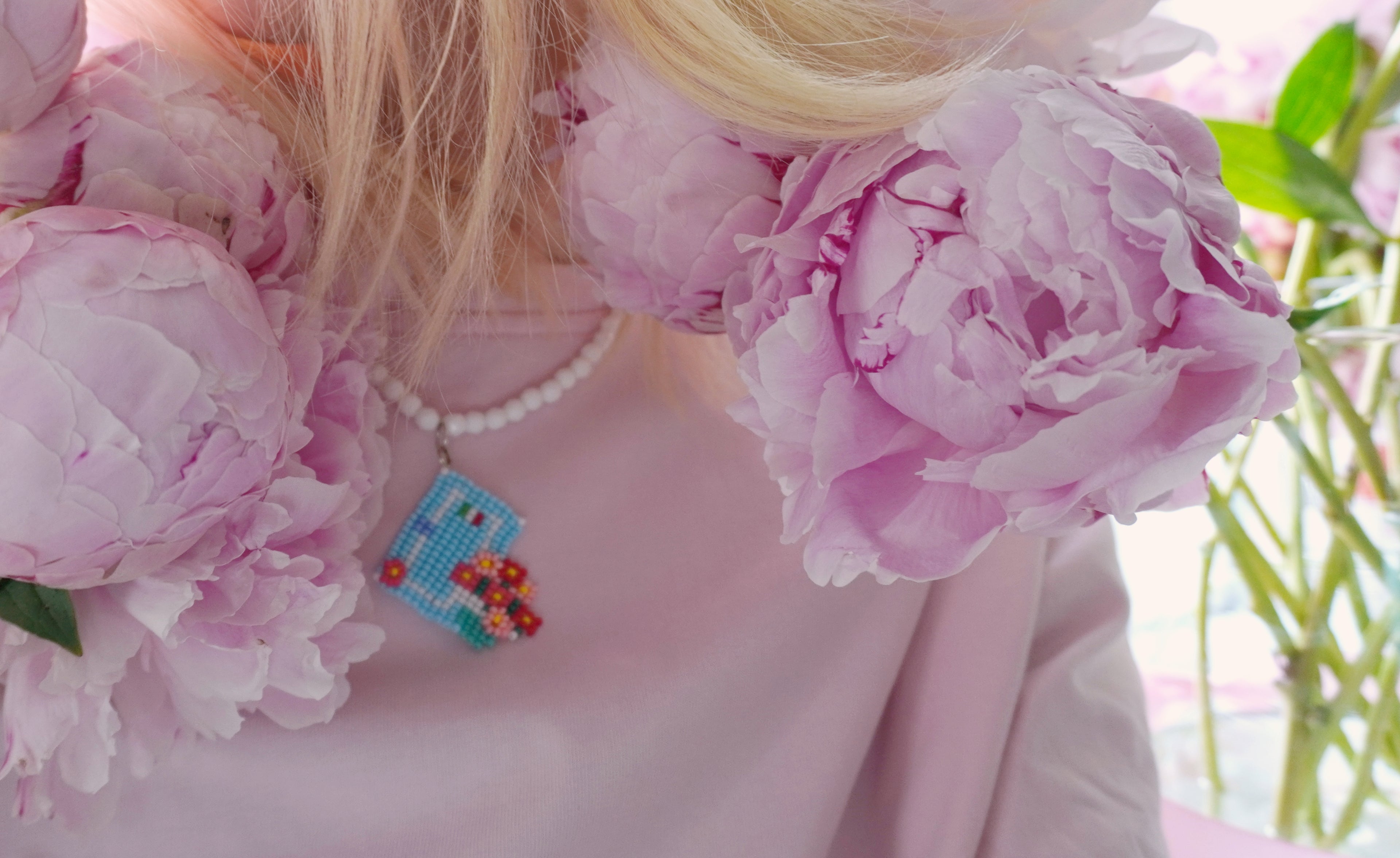 person wearing beaded necklace inspired by Italian houses with geranium flowers and pink t-shirt with peony background