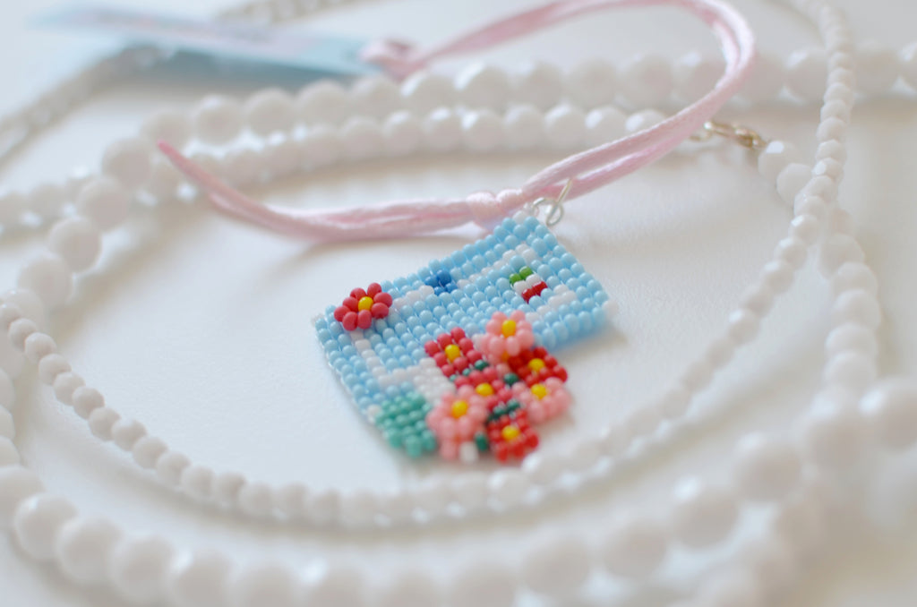 Handmade beaded Italian house necklace with blue door and flowers on a white background.