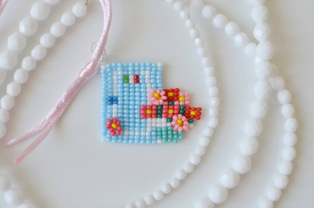 Close-up of a beaded Italian home pendant with pastel blue door and geranium flowers.