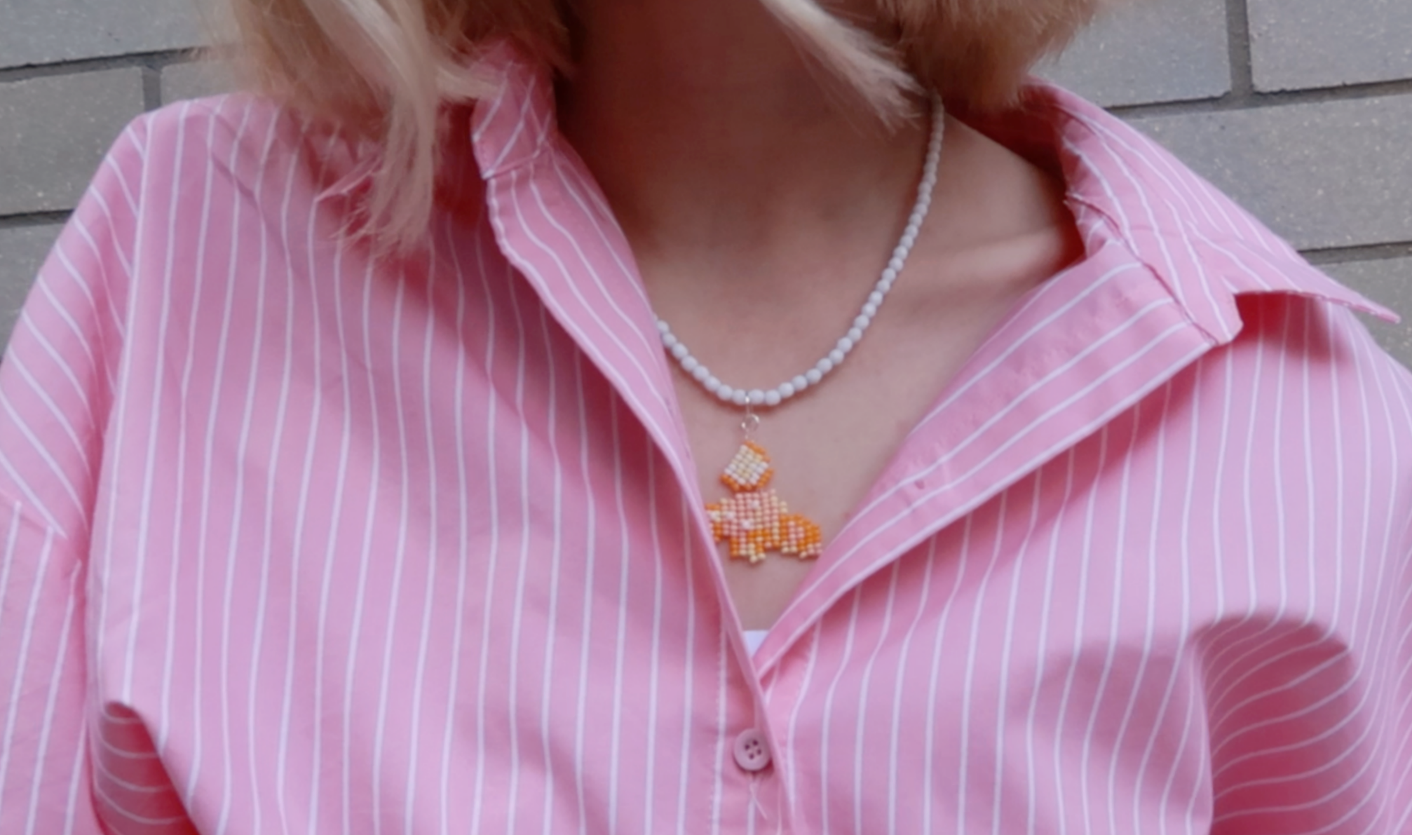 Person wearing a pink striped shirt with a cornetto-inspired beaded necklace against a neutral background.