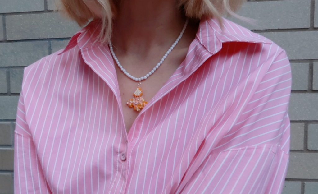 Person wearing a pink striped shirt with a white beaded necklace featuring a cornetto pendant.