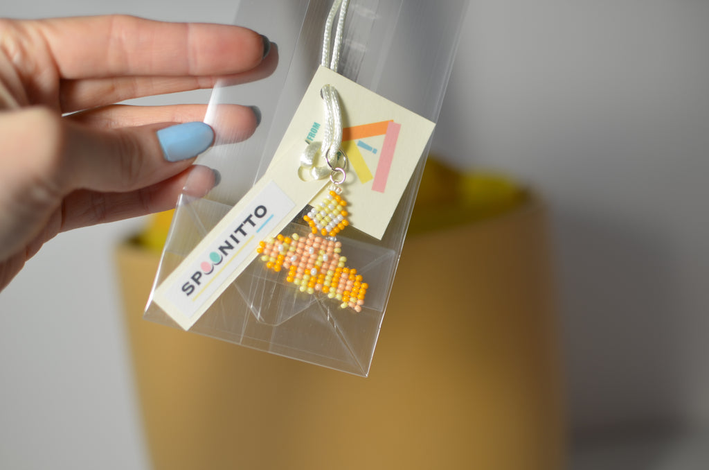 Hand holding a clear bag with a beaded cornetto pendant and SPOONITTO branding.