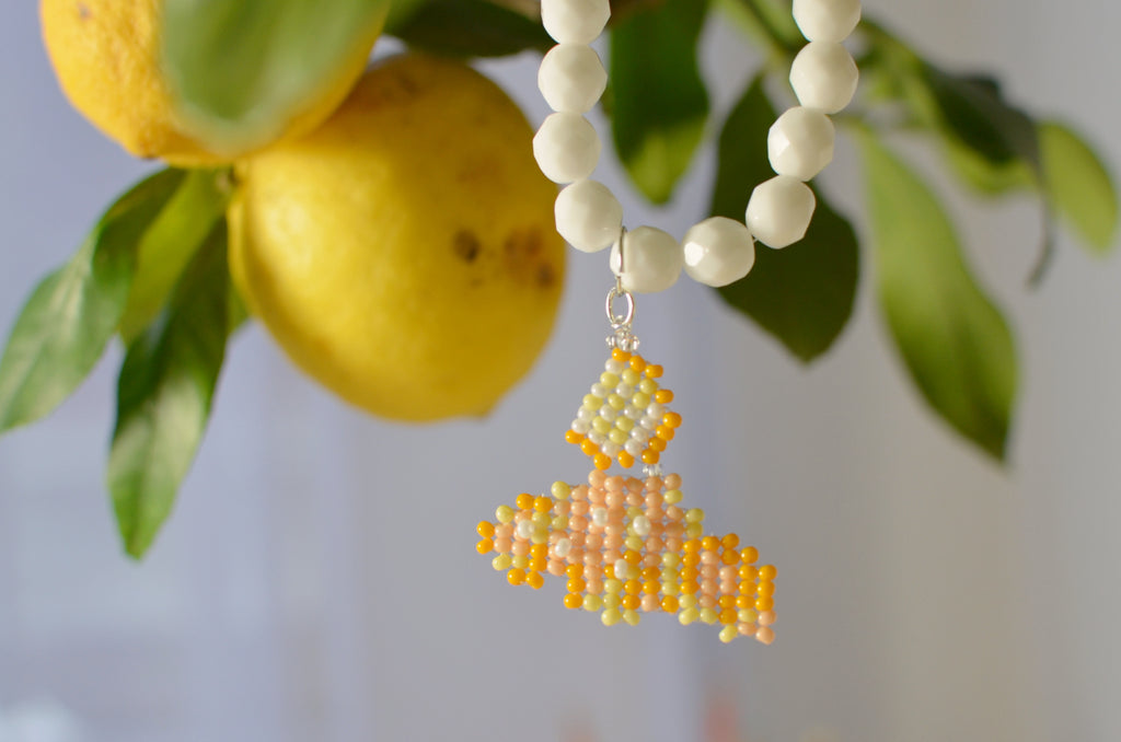 White beaded necklace with a cornetto pendant next to lemons and leaves.