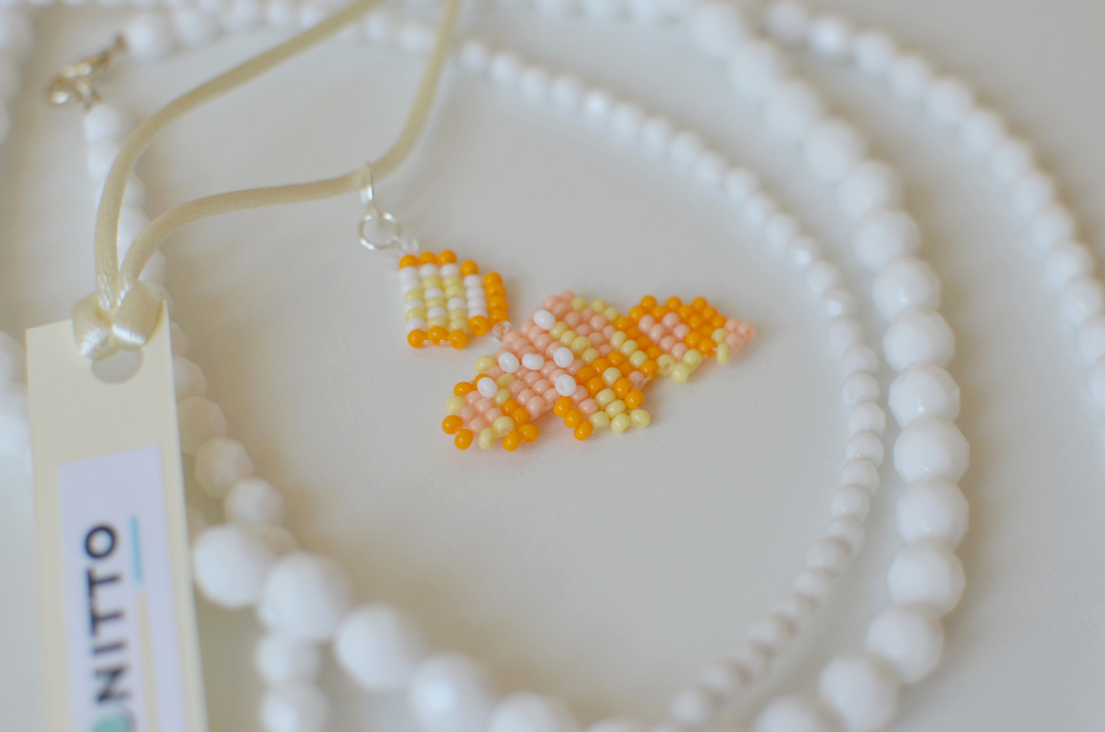White beaded necklace with a cornetto pendant on a white textured surface.