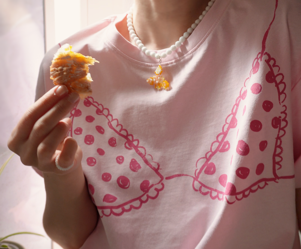 Person wearing a pink t-shirt and croissant inspired necklace holding a small piece of Italian cornetto.