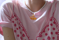 Person wearing a pink shirt with red patterns and italian cornetto beaded necklace.