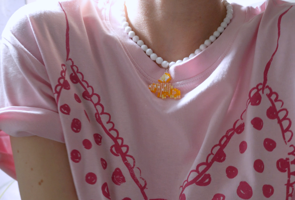 Person wearing a pink shirt with red patterns and italian cornetto beaded necklace.