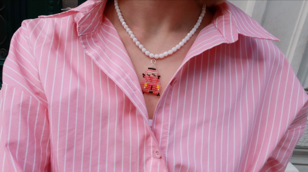 Person wearing a pink striped shirt with a necklace and colorful beaded small car pendant.