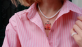 Person wearing a pink striped shirt with a white beaded necklace featuring a red retro car pendant.