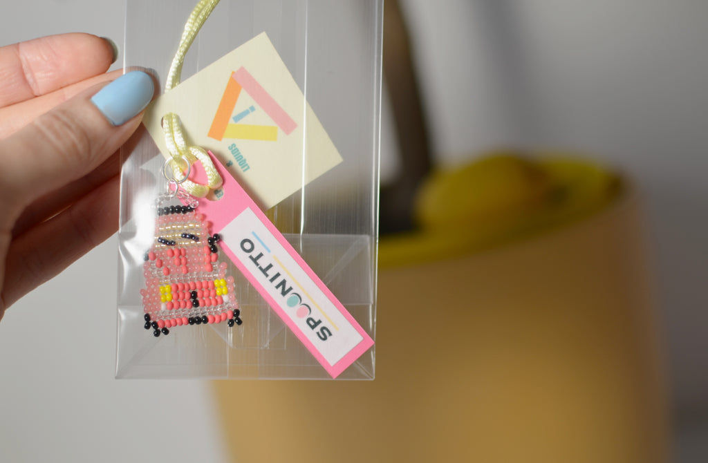 Hand holding a clear bag with a red retro car beaded pendant and SPOONITTO branding.