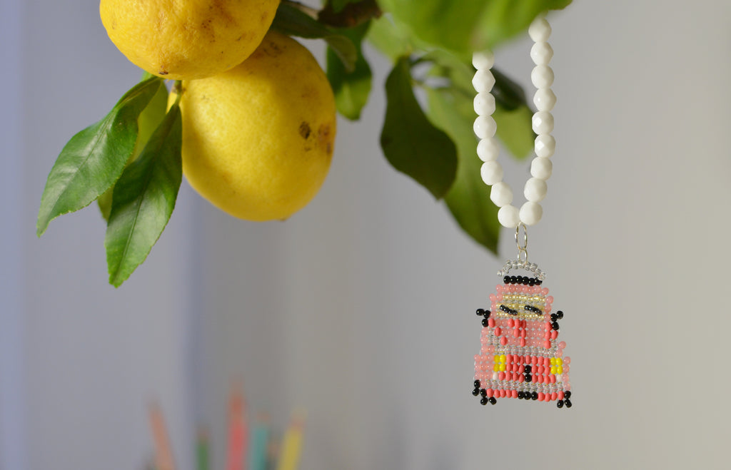 White beaded necklace with a red retro car pendant next to lemons and leaves.