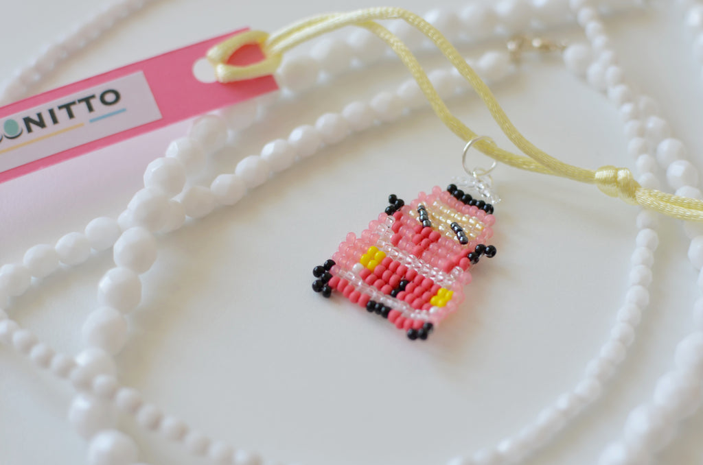 Close-up of a handmade red retro car beaded pendant on a white background.