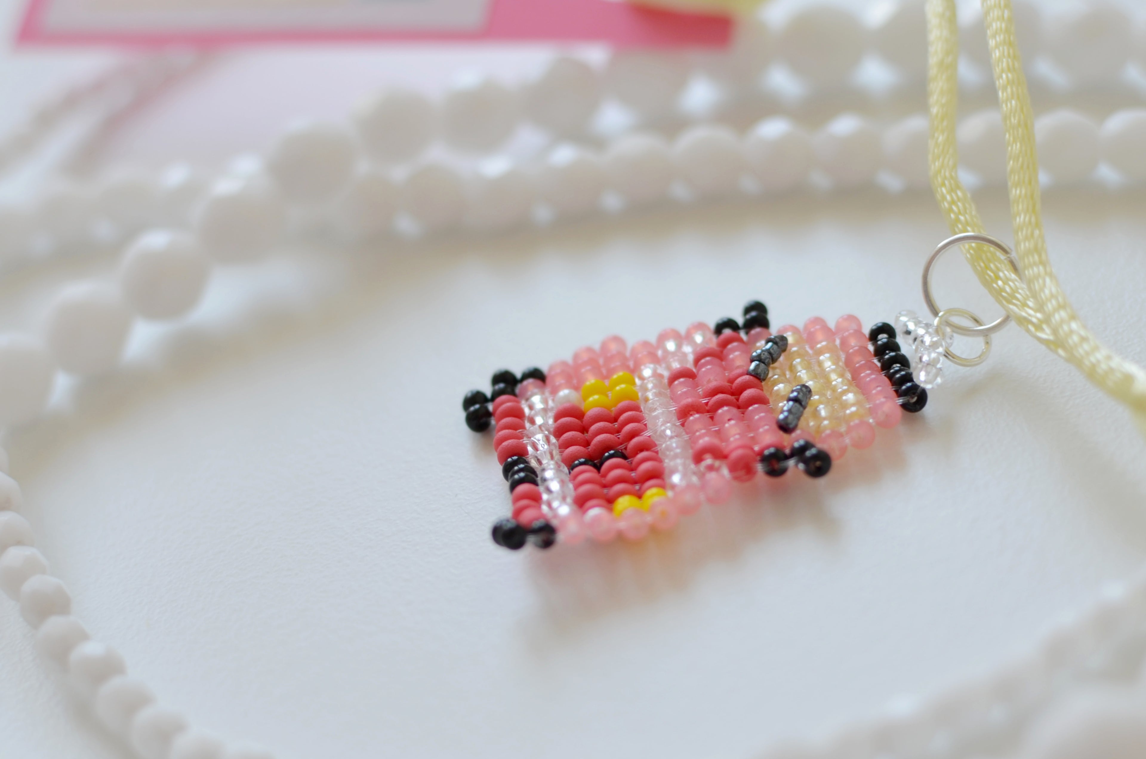 White beaded necklace with a small red car pendant on a white textured surface.
