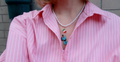 Person wearing a pink striped shirt with a necklace featuring small moka pot and italian flag