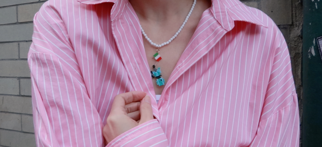 Person wearing a pink striped shirt with a pearl necklace and colorful moka pot pendant with italian flag