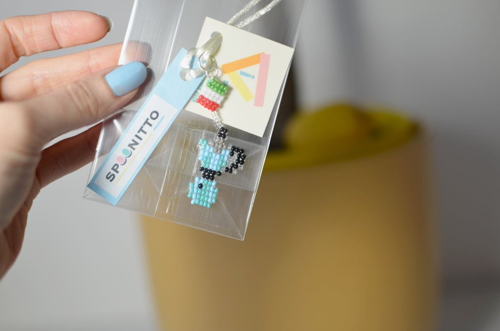 Hand holding a package with blue moka pot beaded pendant and a SPOONITTO label.