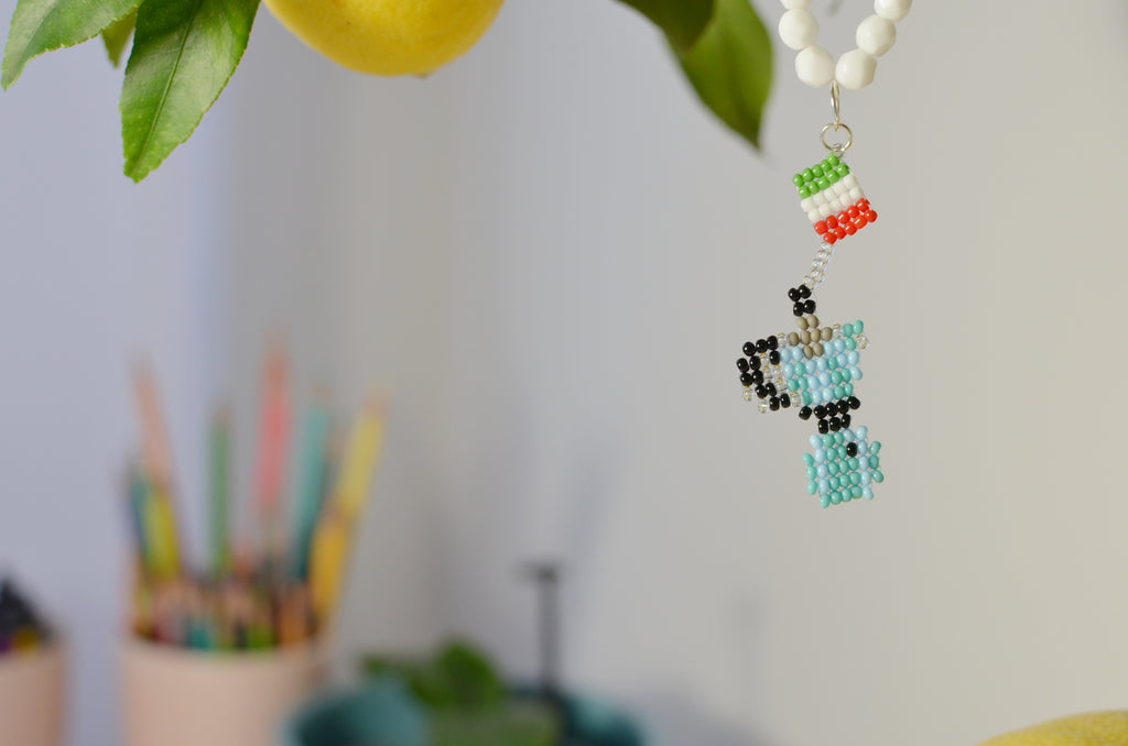 Colorful beaded pastel blue moka pot with a blurred background of pencils and plants