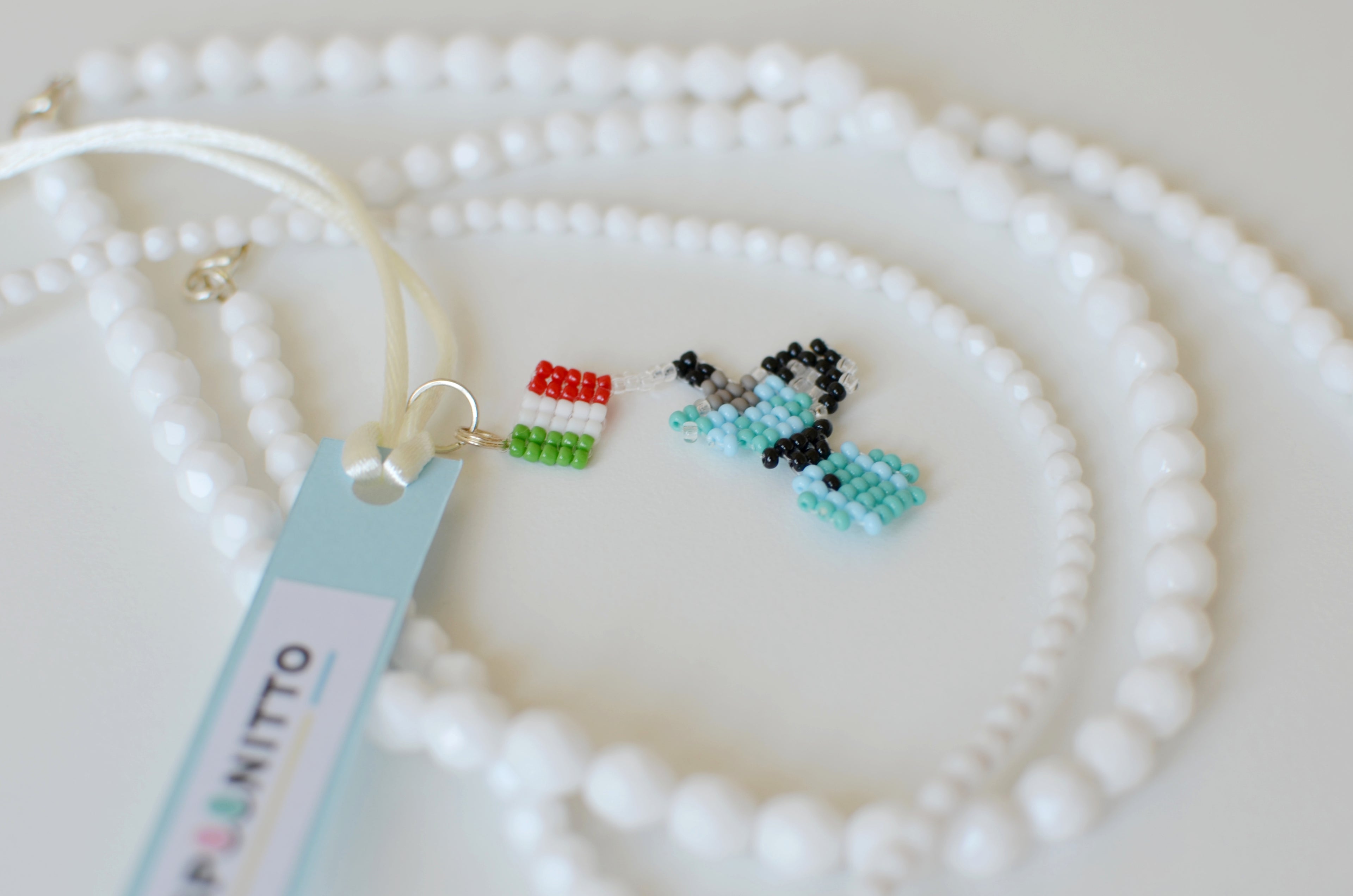 Small beaded moka pot pendant on a white pearl necklace with a visible brand tag.