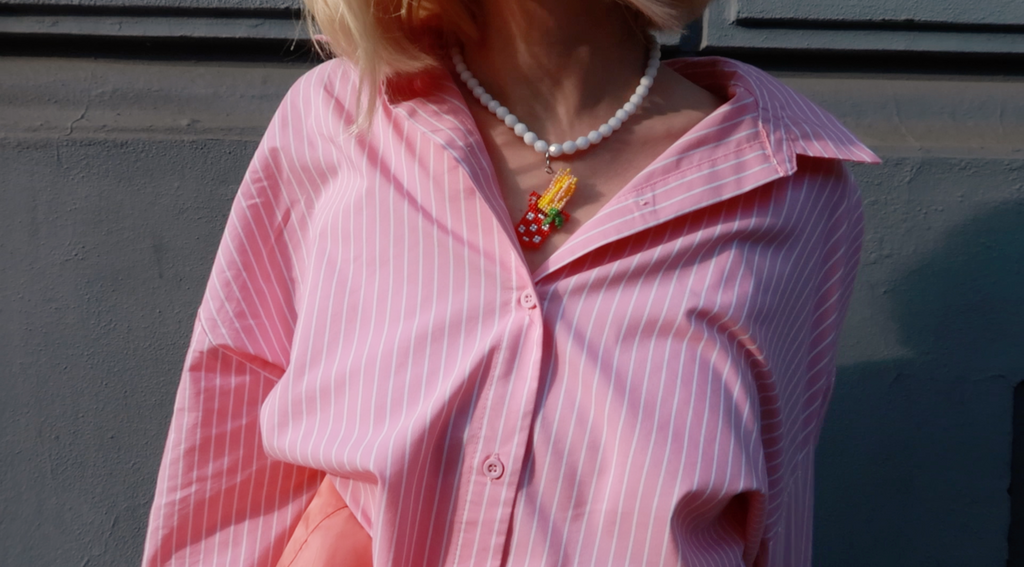 Person wearing a pink striped shirt with a white beaded necklace featuring a spaghetti pot pendant.