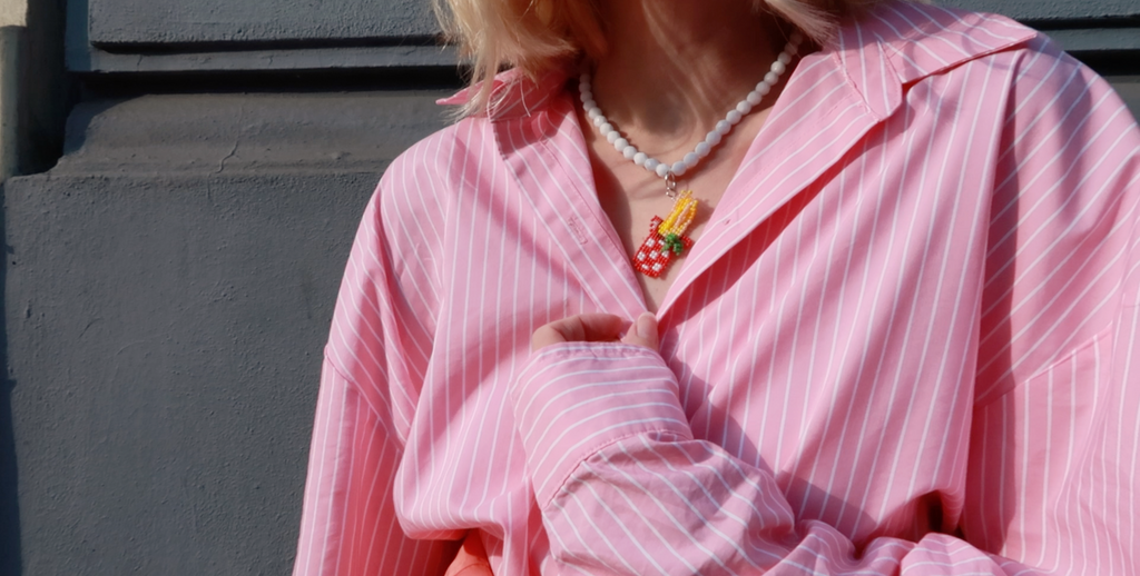 Person wearing a pink striped shirt with a food-inspired spaghetti necklace against a neutral background.