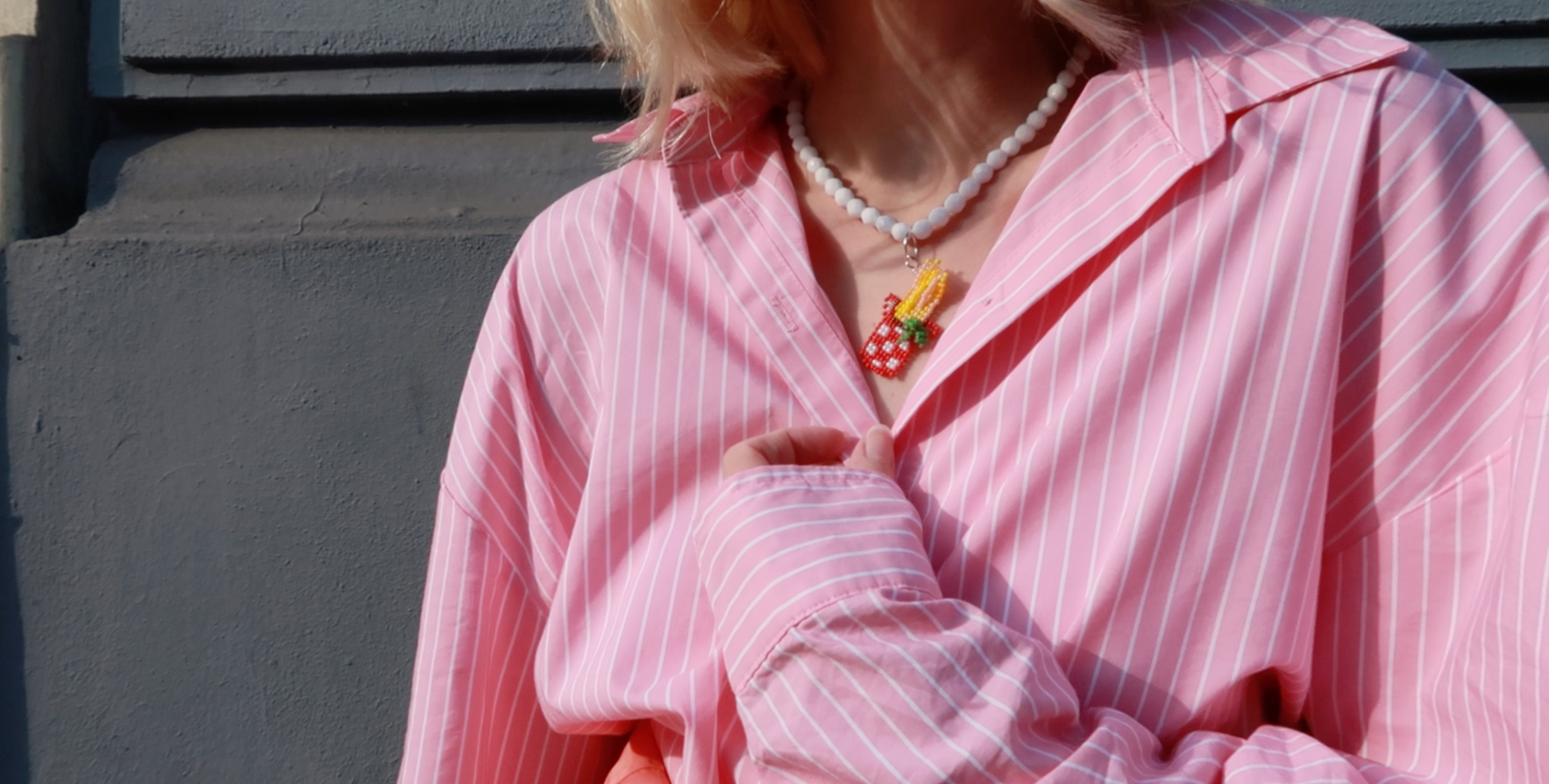 Person wearing a pink striped shirt with a food-inspired spaghetti necklace against a neutral background.