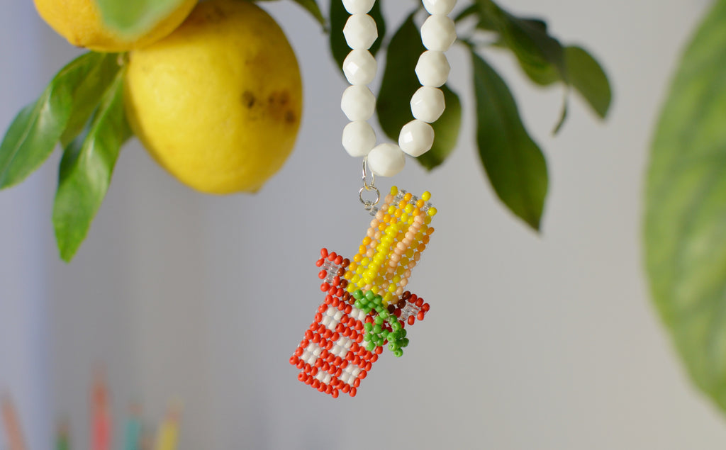 White beaded necklace with a spaghetti pot pendant next to lemons and leaves.