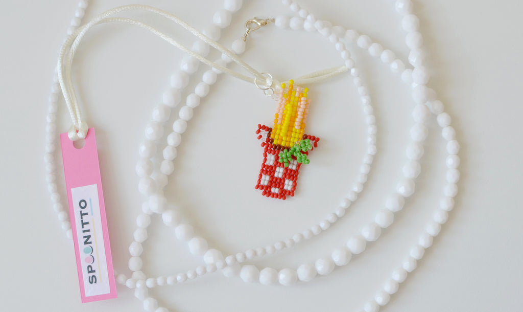 Handmade beaded spaghetti pot necklace with basil on a white background.