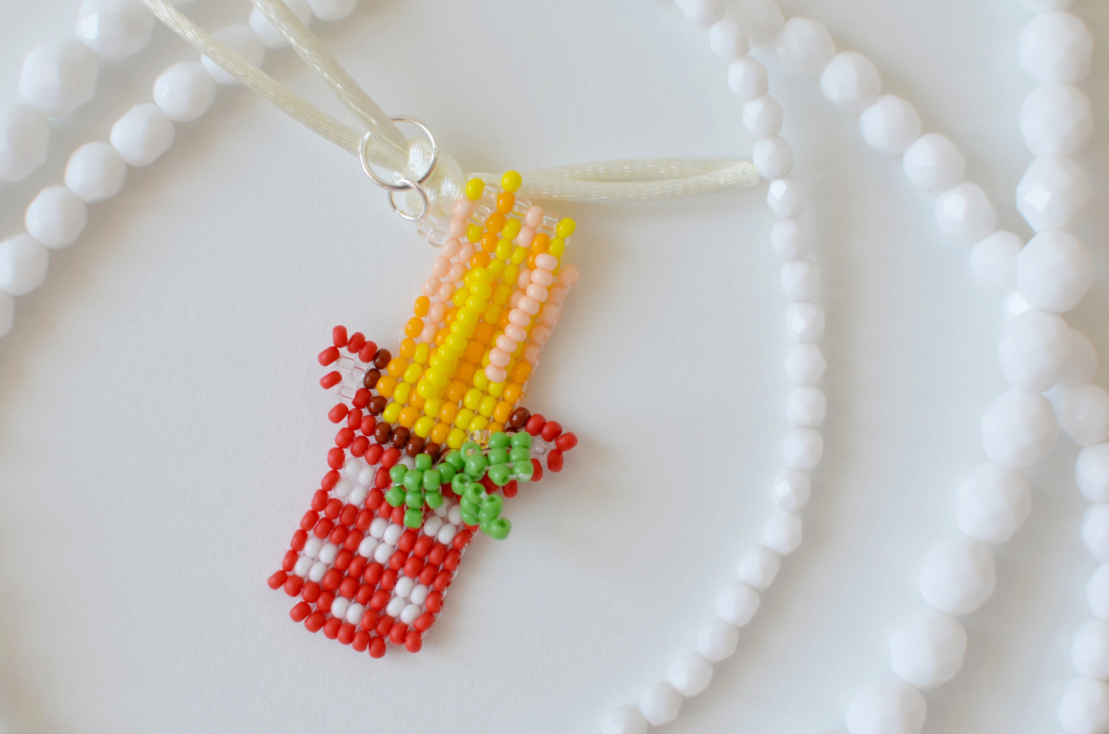White beaded necklace with a spaghetti and basil pendant on a white textured surface.