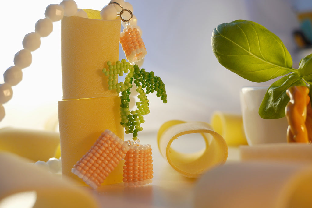 Italian pasta inspired necklace with yellow pasta shapes with green basil leaves on a light background