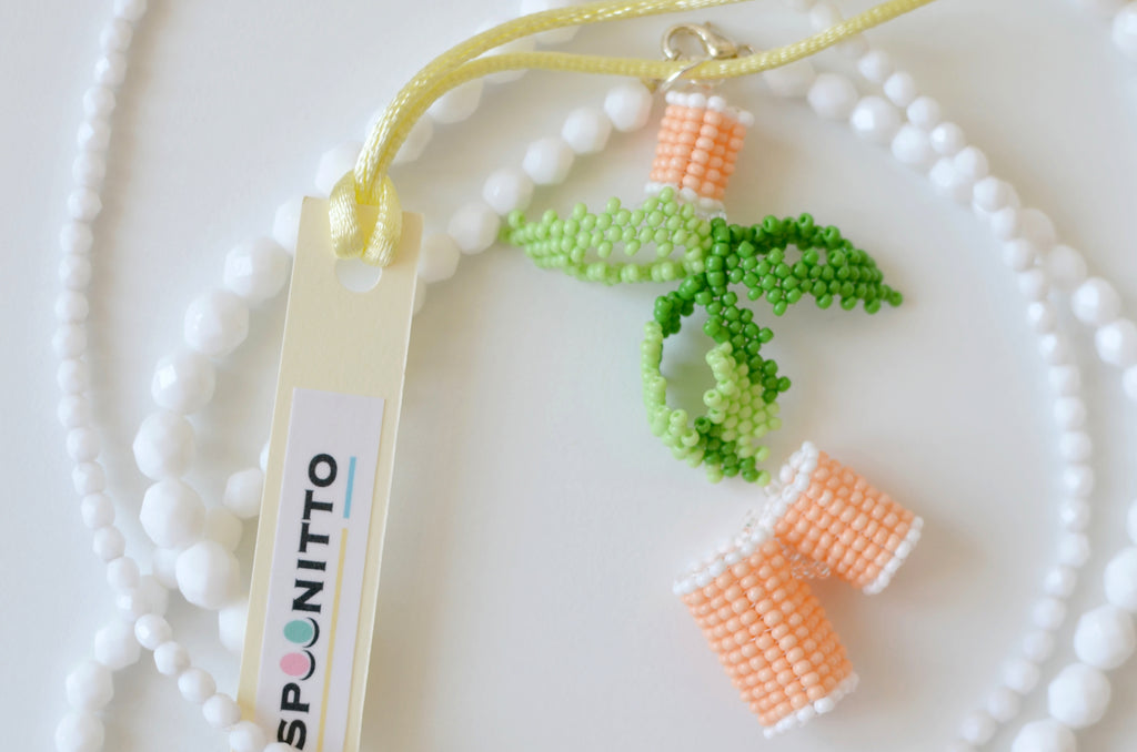 White necklace with beaded pasta and basil leafs pendant on a white background