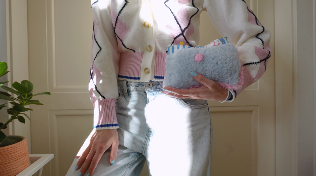 Person wearing a patterned cardigan holding a fluffy blue clutch with a big pink button.