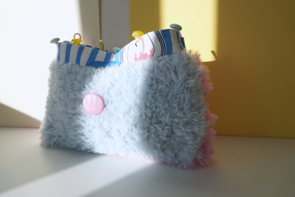 Small handbag with a fluffy pastel blue knitting and pink accents on a light surface.