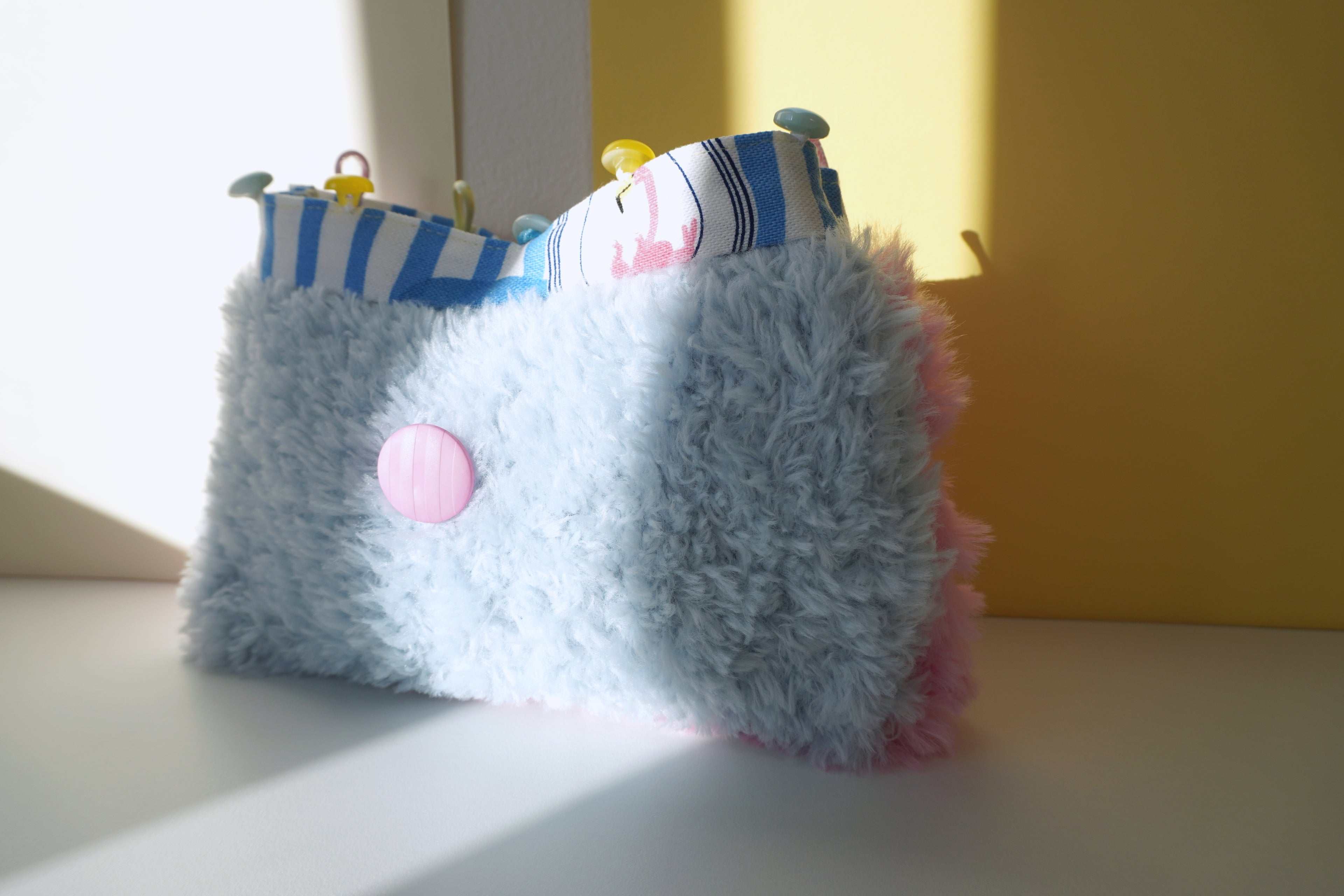 Small handbag with a fluffy pastel blue knitting and pink accents on a light surface.