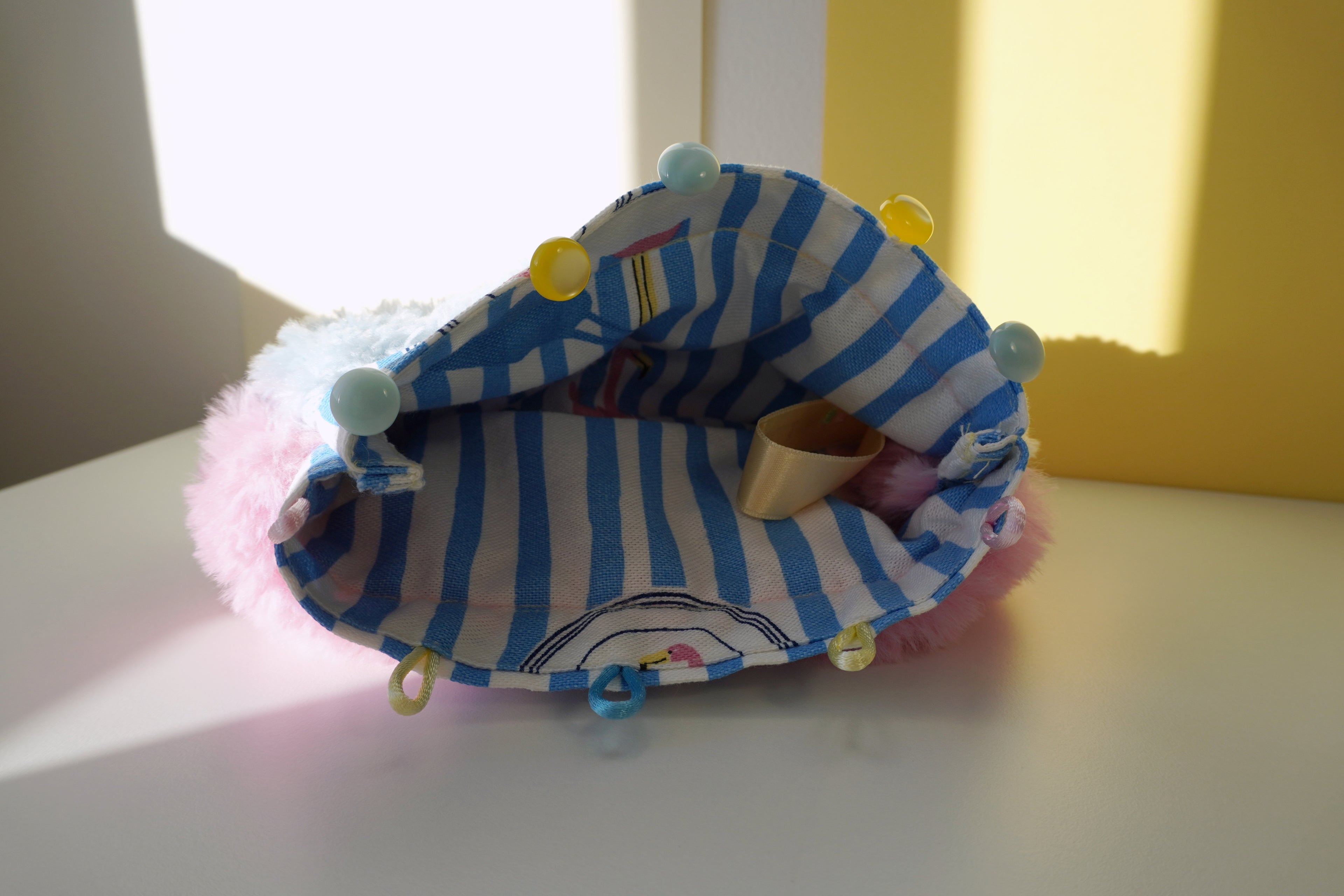 small fluffy bag with a striped lining and yellow and blue buttons