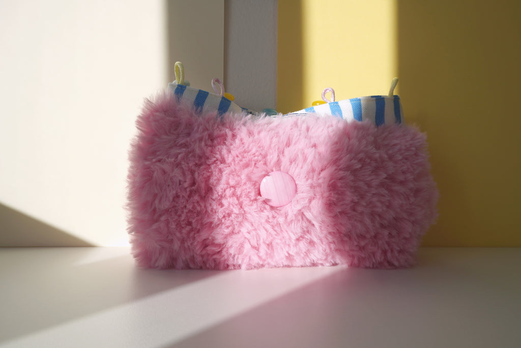 Pink fluffy purse with buttons on a white and yellow surface