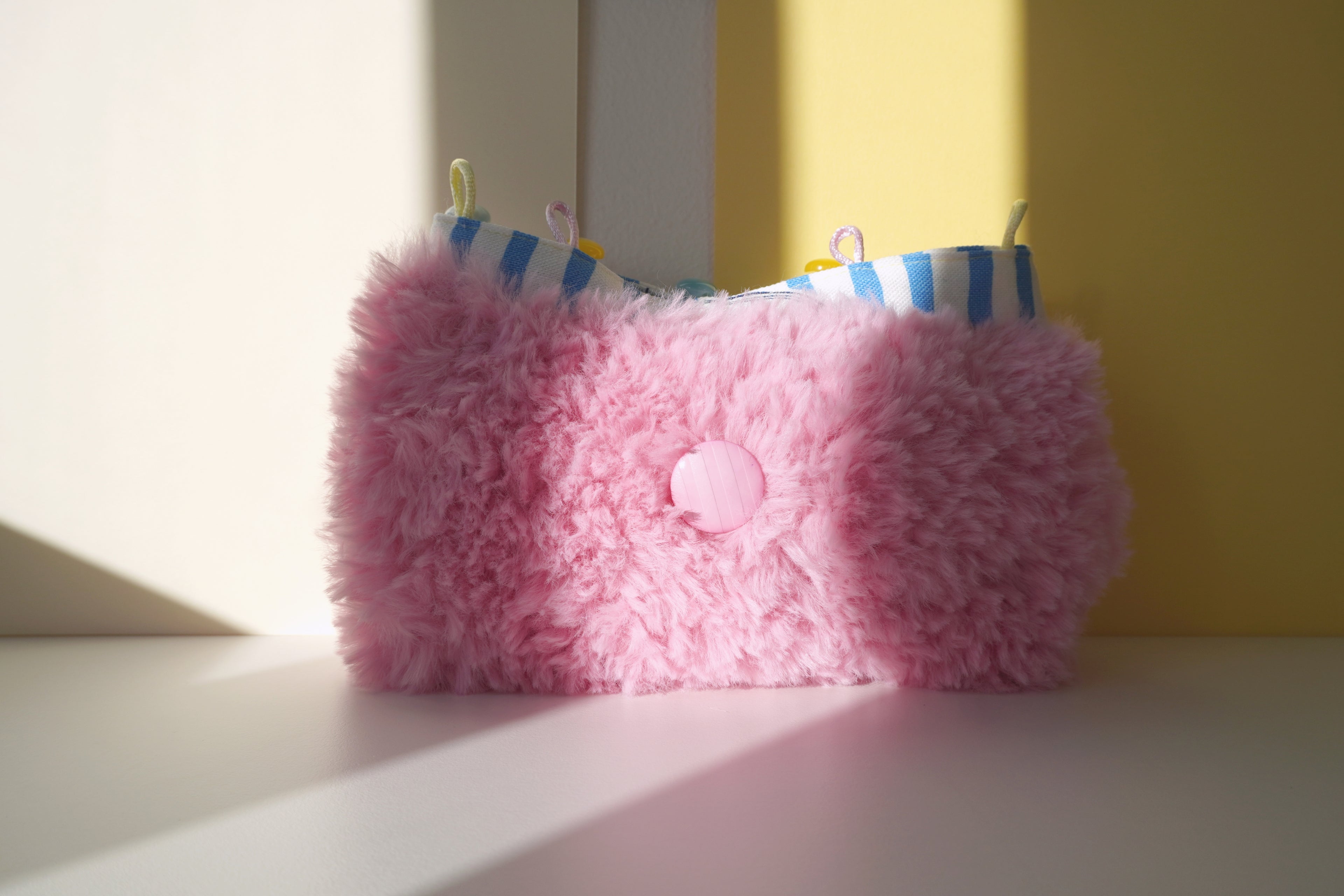 Pink fluffy purse with buttons on a white and yellow surface