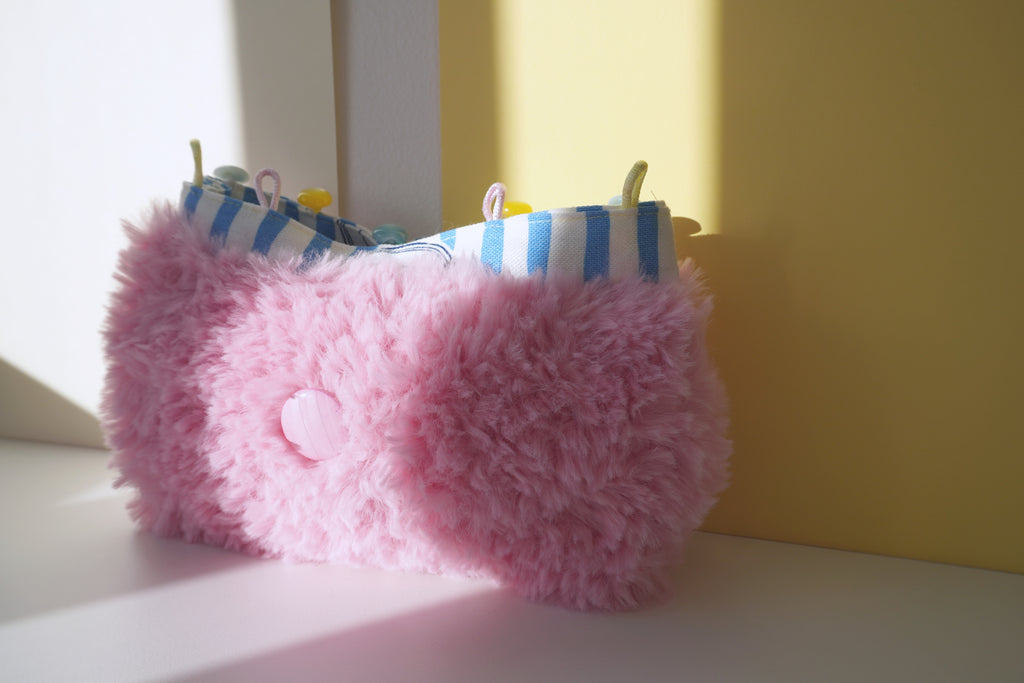 Pink fluffy purse with blue and white lining and a big pink button on a light surface.