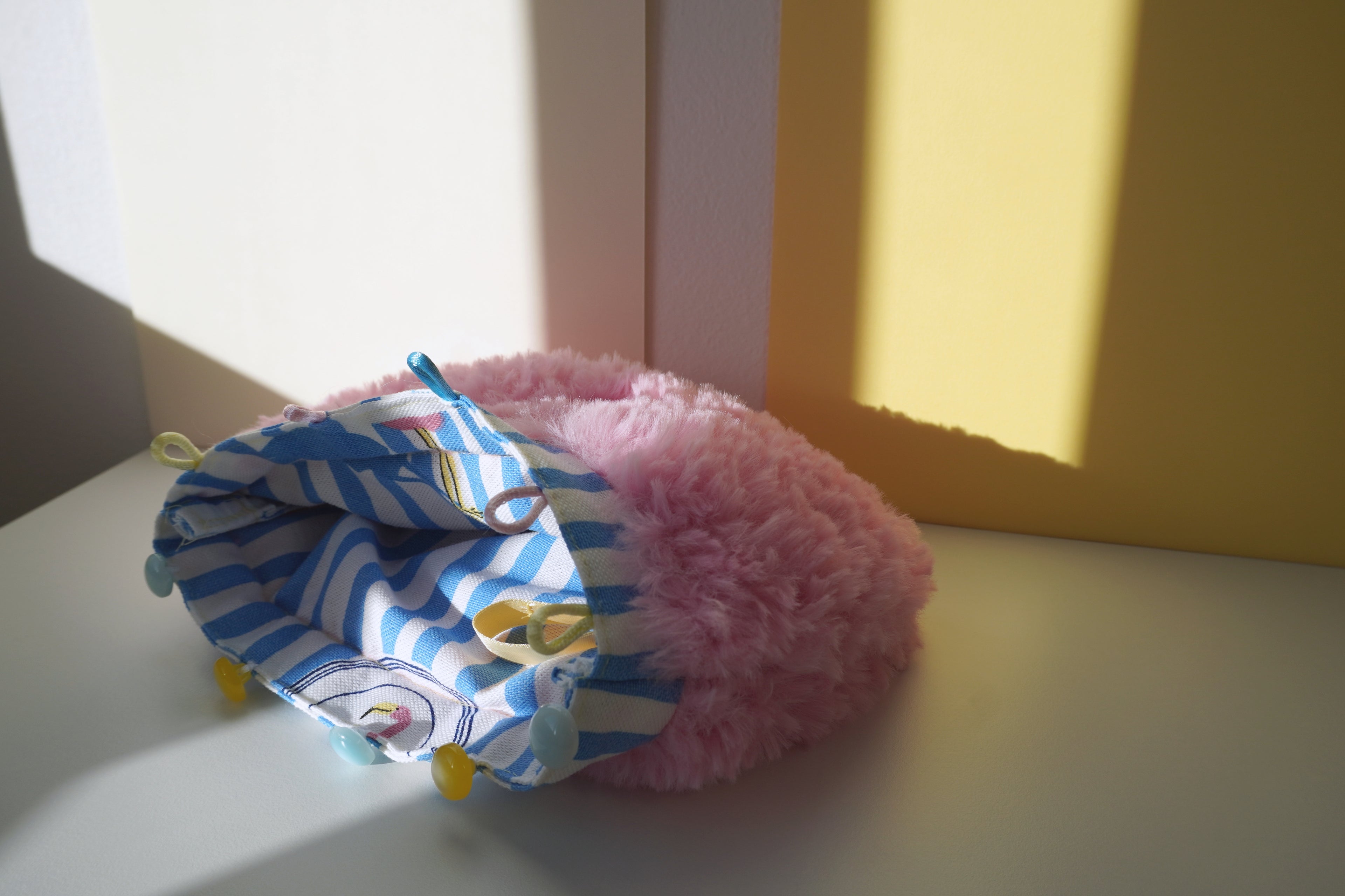 Pink fluffy small purse with a blue and white striped lining on a light surface.
