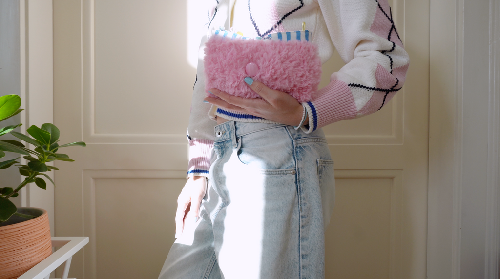 Person holding a pink fluffy small bag in a room with a plant and white wall.